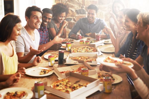A diverse group of friends around a wooden table, sharing pizza and drinks, laughing and chatting.